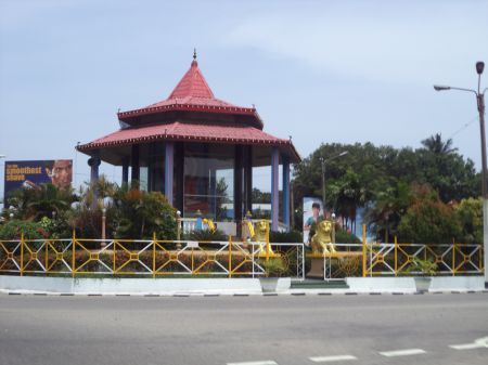A huge statue of Buddha sits in a road junction. 